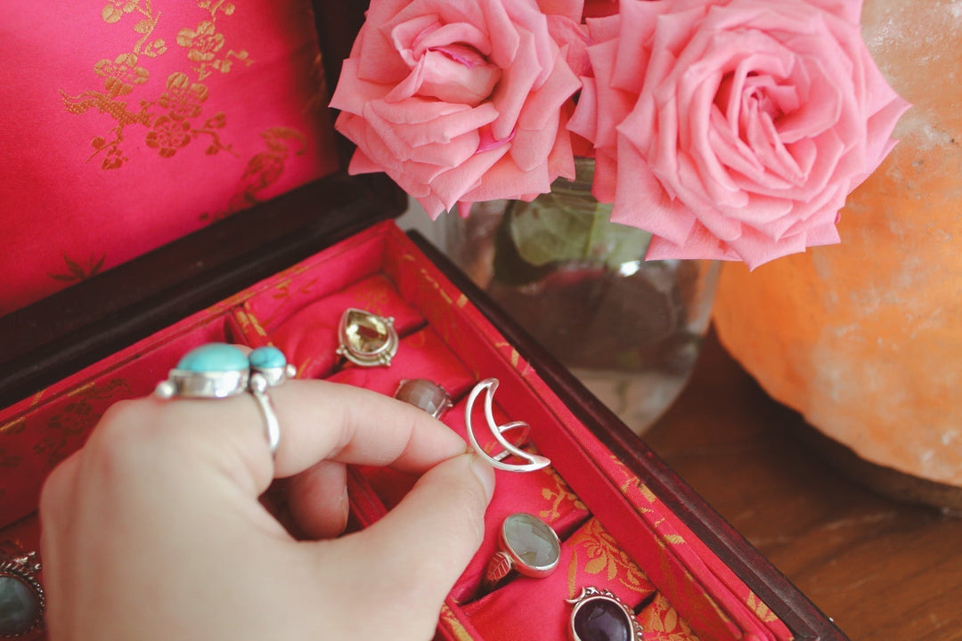 holding a crescent moon sterling silver ring in a red jewelry box surrounded by pink roses